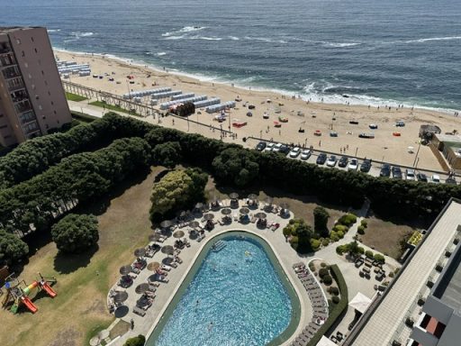 Blick auf den Strand mit Pool, Liegestühlen und Autosparkplatz in der Nähe.