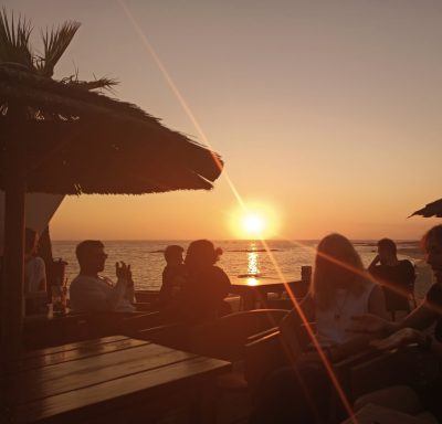 Sonnenuntergang über dem Meer, silhouettierte Personen im Vordergrund.
